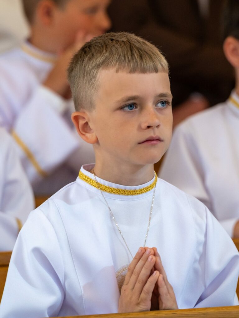 Chłopiec w albie modli się podczas Mszy komunijnej